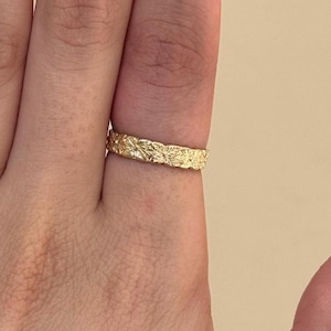 Peut inclure: Une bague en or avec un motif floral. La bague est portée au doigt et a une surface texturée. La bague est de couleur or brillant.