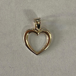 Peut inclure: Un pendentif en forme de cœur doré avec un bord texturé et une boucle pour une chaîne. Le pendentif est en forme de cœur creux, et le métal a une finition brillante. Le pendentif est probablement en or ou plaqué or.