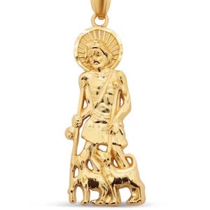 May include: A gold-colored pendant featuring a religious figure with a halo, staff, and two sheep. The pendant has a detailed design and a loop at the top for a chain. The figure is standing, and the sheep are at the figure's feet.