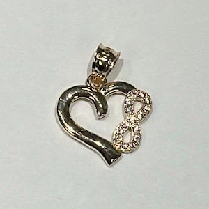 Peut inclure: Pendentif doré en forme de cœur avec un symbole infini orné de petits pierres précieuses transparentes. Le pendentif est doté d'une bélière pour l'attacher à une chaîne.
