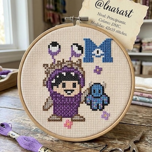 May include: A circular wooden embroidery hoop containing a cross-stitch pattern of a purple monster character, a small blue monster, and a large blue letter M. A paper note attached to the top reads @lnarart, Nivel: Principiante, Colores: DMC, Medidas: 42x55 stitches.