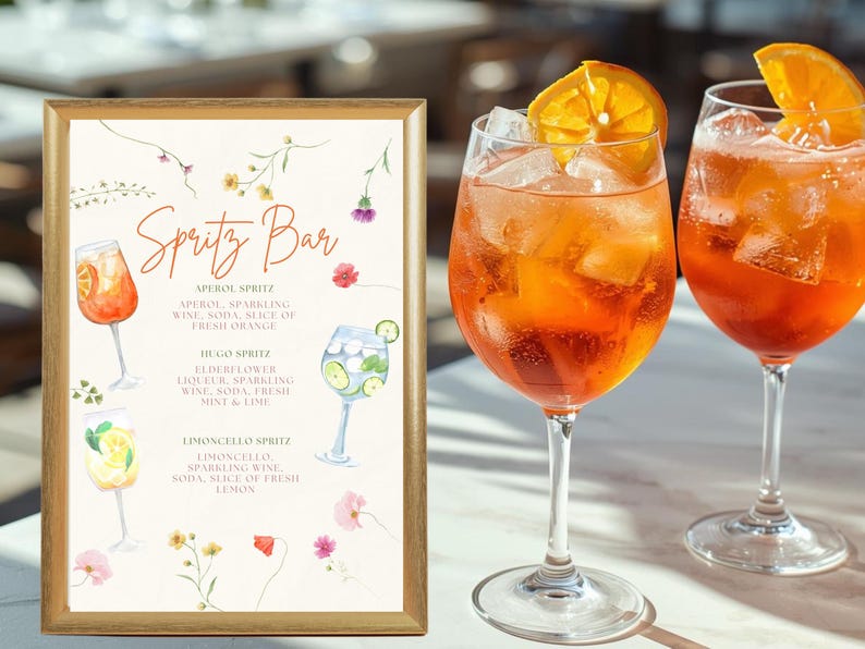 Puede incluir: Un letrero con texto "Spritz Bar" e ilustraciones de c&oacute;cteles, junto a dos copas de c&oacute;cteles spritz de color naranja. El letrero detalla las recetas de spritz Aperol, Hugo y Limoncello. Los c&oacute;cteles tienen hielo y rodajas de naranja.