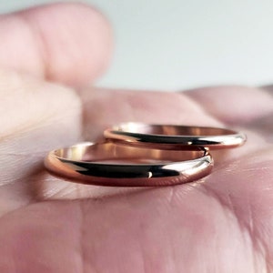 Shiny 14k rose gold wedding rings held in hand. Classic traditional polished domed wedding band set. 3mm and 2mm D-shaped half round court profile rings.