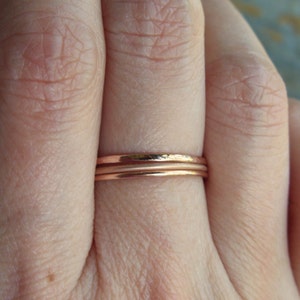 May include: Three thin rose gold stacking rings. The rings are smooth and have a hammered texture.