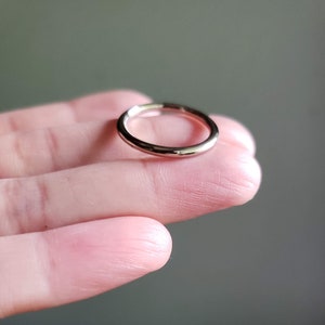 May include: A simple silver band ring, shown on a finger.