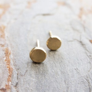 May include: A pair of gold-toned stud earrings with round, slightly textured discs.