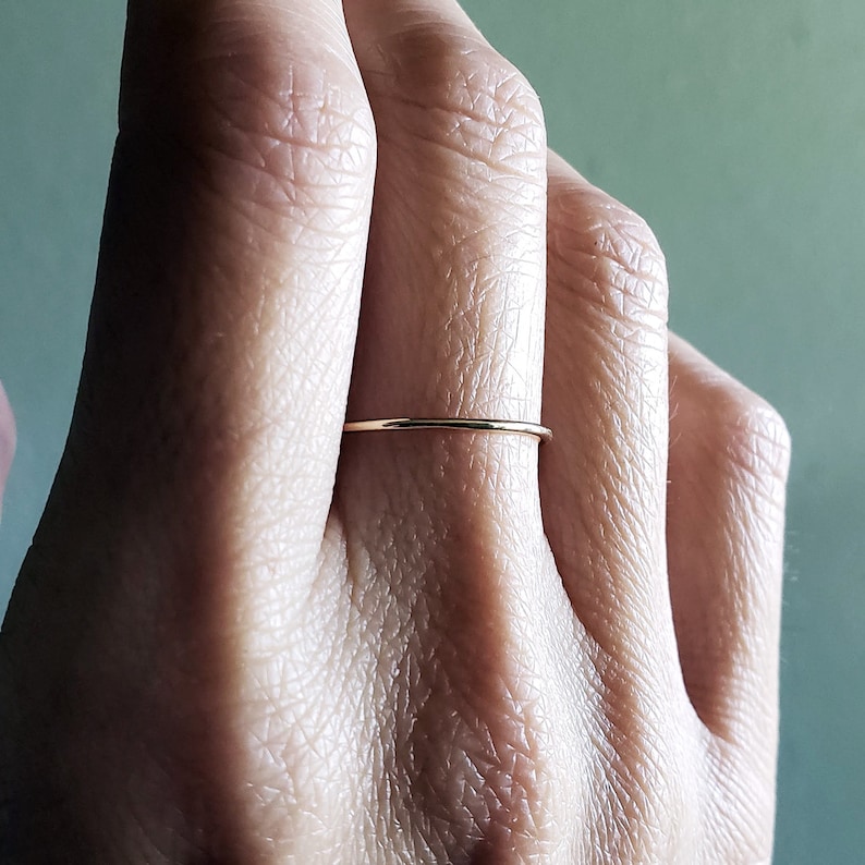 Pu&ograve; includere: Un anello sottile in oro indossato su un dito.