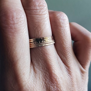 Pu&ograve; includere: Un set di quattro anelli impilabili dorati. Gli anelli sono sottili e delicati, con una texture martellata. Gli anelli sono indossati su un dito.