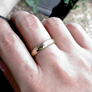 4mm heavily hammered 14k yellow gold domed wedding band worn on finger, shown on woman's hand.