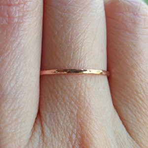 May include: A thin, hammered rose gold band ring worn on a finger.