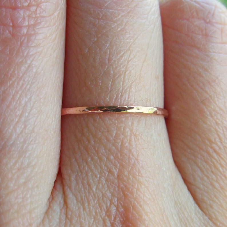 May include: A thin, hammered rose gold band ring worn on a finger.