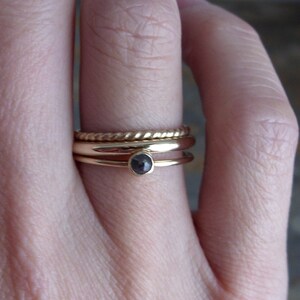 May include: A gold ring set with a black gemstone, worn on a finger with three other gold bands.