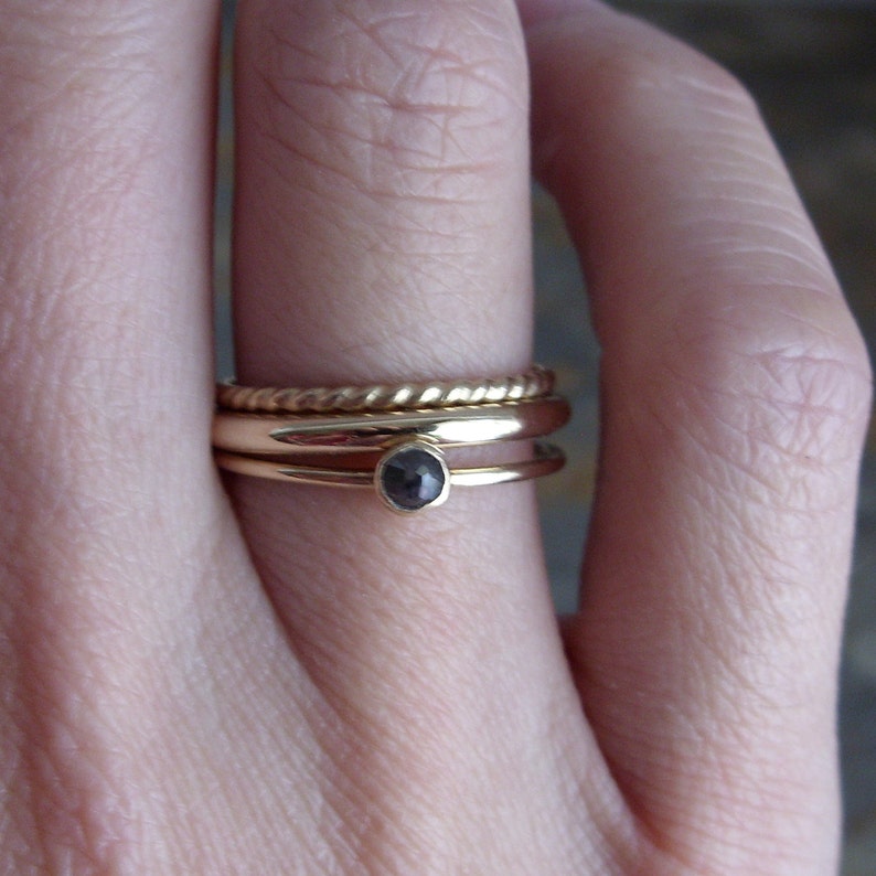 May include: A gold ring set with a black gemstone, worn on a finger with three other gold bands.