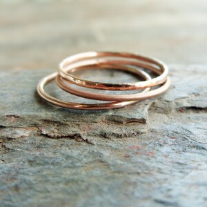 May include: Three thin rose gold rings stacked on top of each other. The rings are smooth and have a slightly hammered texture.