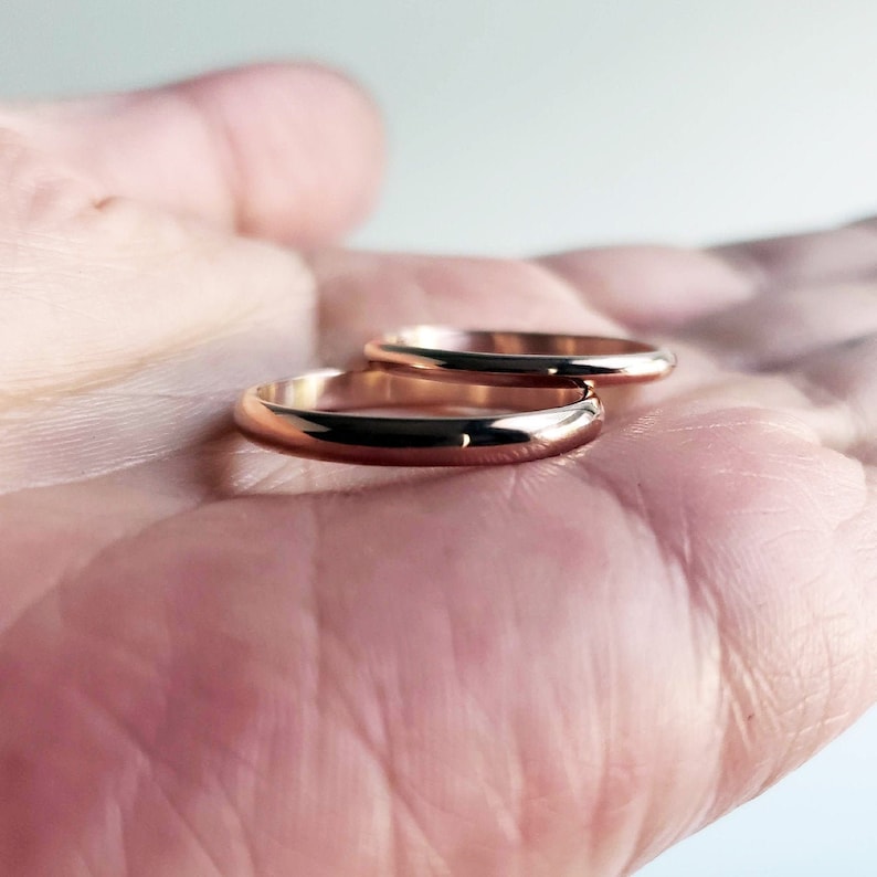 Shiny 14k rose gold wedding rings held in hand. Classic traditional polished domed wedding band set. 3mm and 2mm D-shaped half round court profile rings.