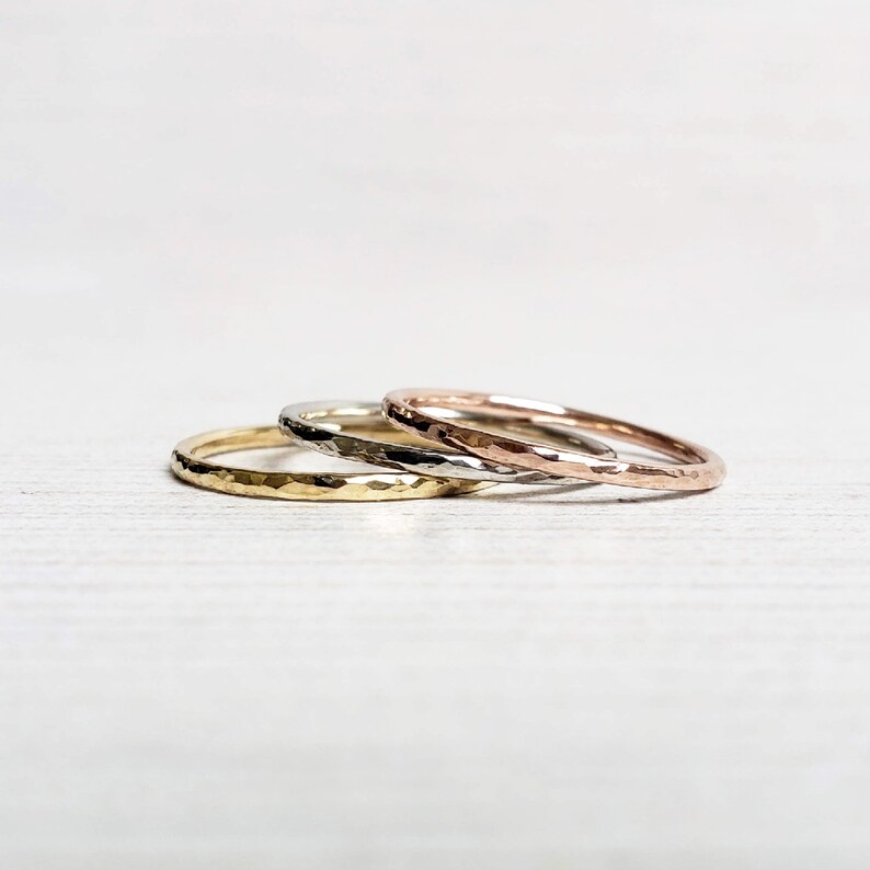 Op de afbeelding: Drie gehamerde metalen ringen in goud, zilver en ros&eacute;goud. De ringen zijn op elkaar gestapeld en tonen hun verschillende kleuren en texturen. De ringen zijn eenvoudig en elegant, geschikt voor dagelijks gebruik.