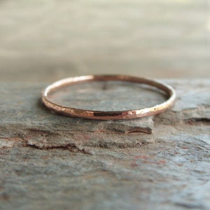 May include: A thin, hammered rose gold band ring. The ring is simple and delicate, with a smooth, polished finish.