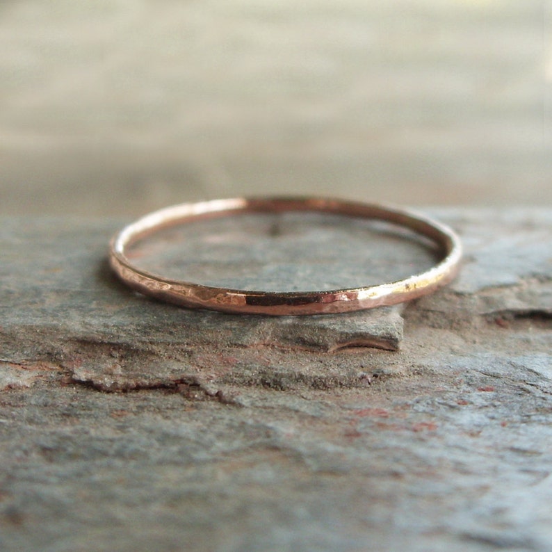 May include: A thin, hammered rose gold band ring. The ring is simple and delicate, with a smooth, polished finish.