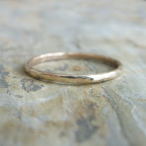 Op de afbeelding: Een gehamerde gouden ring met een getextureerd oppervlak. De ring is dun en heeft een eenvoudig, elegant ontwerp. De ring is geplaatst tegen een neutrale achtergrond.