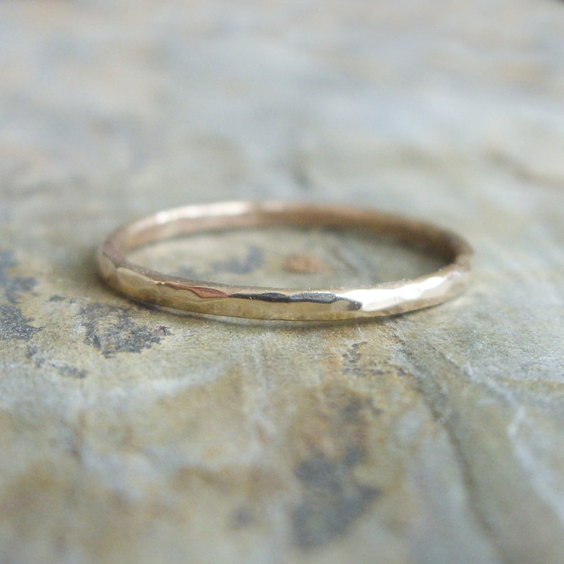 Op de afbeelding: Een gehamerde gouden ring met een getextureerd oppervlak. De ring is dun en heeft een eenvoudig, elegant ontwerp. De ring is geplaatst tegen een neutrale achtergrond.