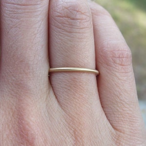 Op de afbeelding: Een close-up van een dunne, goudkleurige ring. De ring heeft een eenvoudig bandontwerp, waarschijnlijk gemaakt van goud of een goudkleurig metaal. De ring zit om een vinger, wat suggereert dat hij als sieraad wordt gedragen. De minimalistische stijl van de ring maakt hem geschikt voor dagelijks gebruik.