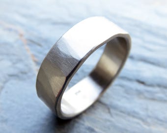 May include: A silver-colored ring with a flat top and faceted edges. The ring has a brushed metal finish and a simple, modern design. The ring is likely made of sterling silver or a similar metal. The ring is a piece of jewelry.