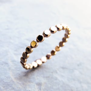 May include: A gold ring with a beaded design. The ring is made of small, round beads that are connected together to form a continuous band.