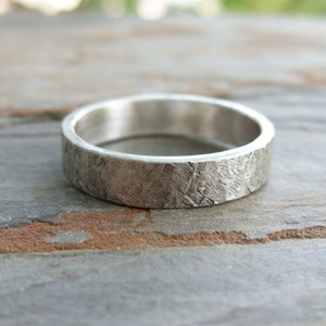 Puede incluir: Un anillo de banda de plata con un acabado texturizado. El anillo es ancho y tiene un aspecto martillado.