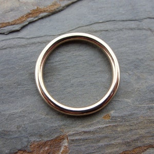 May include: A simple gold band ring, shown on a gray textured surface.