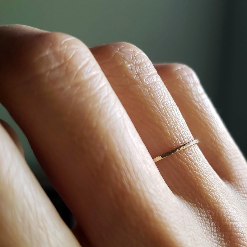 Pu&ograve; includere: Un sottile anello a fascia d'oro con una texture martellata indossato su un dito.