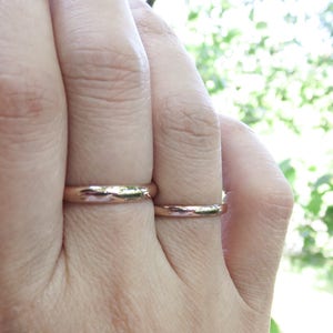 Shiny 14k rose gold wedding rings worn on hand. Classic traditional polished domed wedding band set shown on finger. 3mm and 2mm D-shaped half round court profile rings.