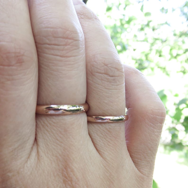 Shiny 14k rose gold wedding rings worn on hand. Classic traditional polished domed wedding band set shown on finger. 3mm and 2mm D-shaped half round court profile rings.