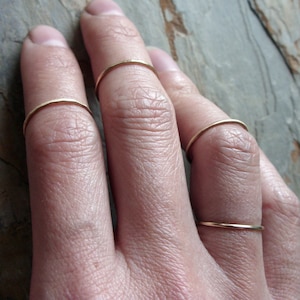 May include: A hand wearing four thin gold rings on different fingers.