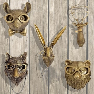 Puede incluir: Cinco esculturas doradas de cabezas de animales con gafas y vello facial. Las esculturas están montadas sobre un fondo de panel de madera. Los animales incluyen un conejo, un ciervo, un oso y otros dos animales.
