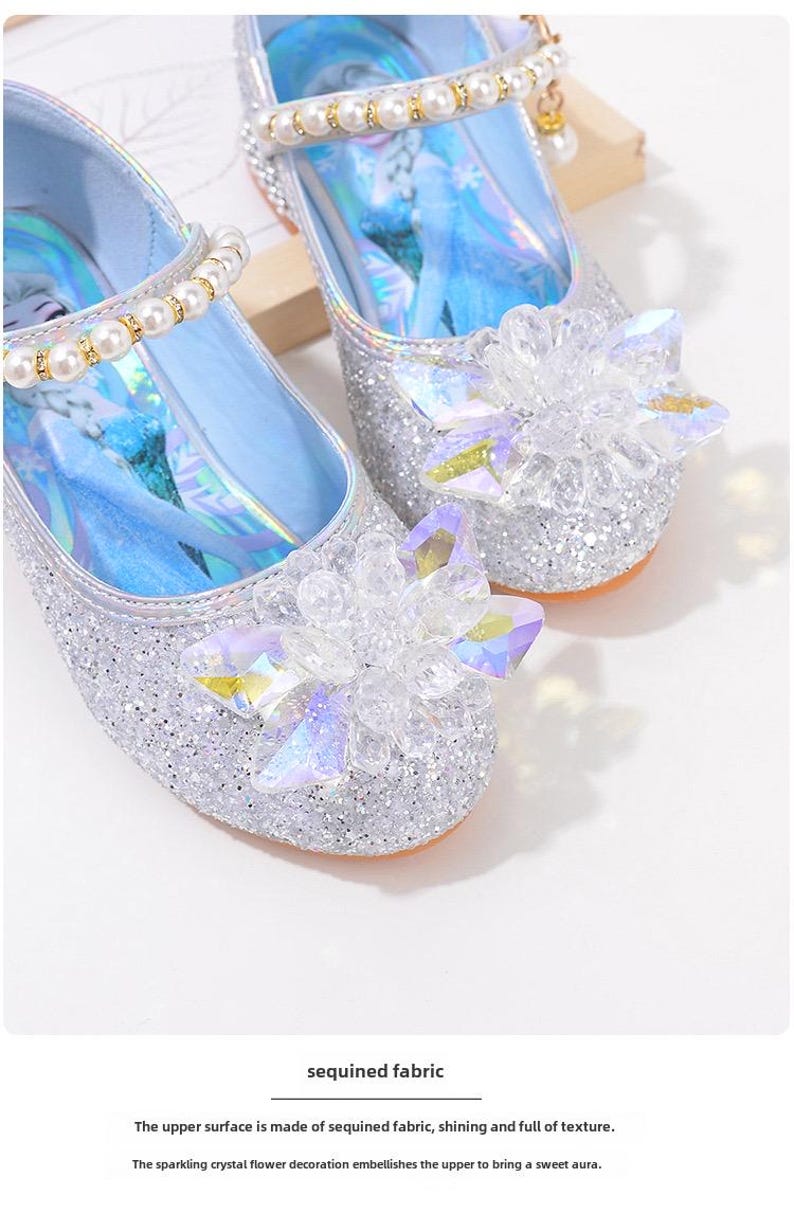 Puede incluir: Zapatos plateados de tela de lentejuelas con adornos de flores de cristal. Los zapatos tienen una correa adornada con perlas y un interior azul claro. El texto de la imagen dice "sequined fabric".