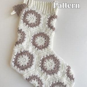 May include: A crocheted Christmas stocking in white with a brown floral design. The stocking features a ribbed cuff and a hanging loop. The words "Crochet Pattern" are displayed in the upper right corner.