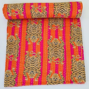 Peut inclure: Une couverture roulée avec un motif de tigre répété sur un fond rayé. Les rayures alternent entre l'orange et le rose. Les tigres sont de couleur beige avec des rayures noires. La couverture est en matière douce et a des coutures blanches.