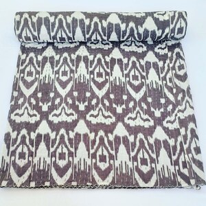 May include: A rolled-up, patterned quilt in shades of gray and off-white. The quilt features a repeating geometric design with visible stitching. The fabric is folded over, revealing the pattern on the rolled edge. The quilt is on a white background.