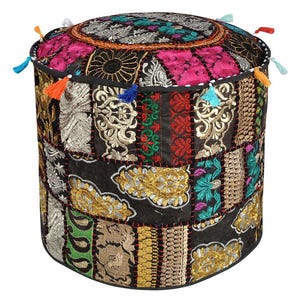 Puede incluir: Un puf redondo de patchwork con base negra y parches bordados coloridos. La parte superior presenta parches rosas, turquesas y plateados, mientras que los lados muestran diseños dorados, rojos y verdes. Pequeñas borlas de varios colores adornan los bordes.