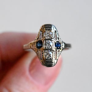 May include: A vintage art deco ring with a filigree design featuring three round diamonds and two blue sapphires.
