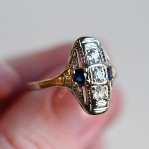 May include: A silver ring with a geometric design featuring blue sapphires and clear diamonds.