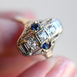 May include: A vintage ring with a geometric design featuring four blue sapphires and four clear diamonds set in a gold and silver band.