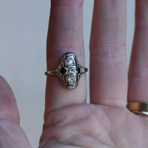May include: A silver ring with a geometric design featuring a row of small diamonds and two black sapphires.