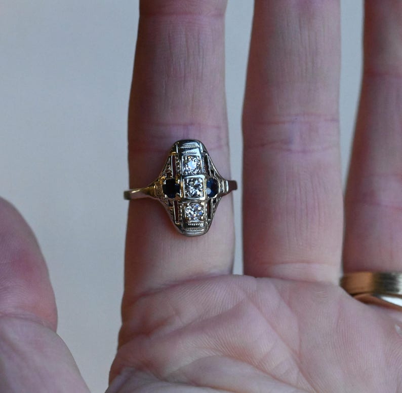 May include: A silver ring with a geometric design featuring a row of small diamonds and two black sapphires.
