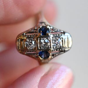 May include: A vintage ring with a delicate filigree design featuring two blue sapphires and two round diamonds.