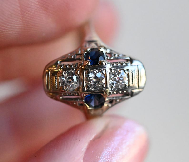 May include: A vintage ring with a delicate filigree design featuring two blue sapphires and two round diamonds.