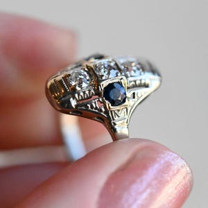 May include: A vintage ring with a central dark blue sapphire surrounded by smaller diamonds set in a delicate filigree design.