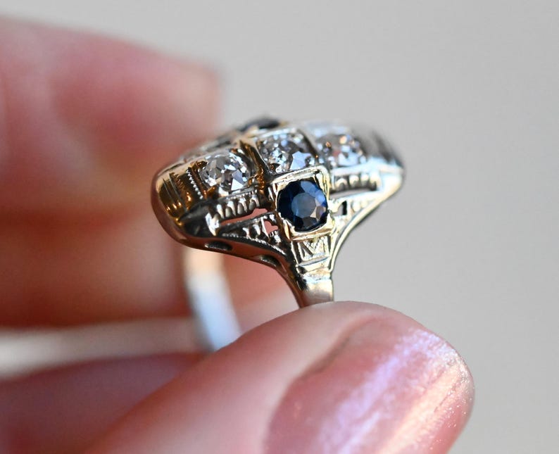 May include: A vintage ring with a central dark blue sapphire surrounded by smaller diamonds set in a delicate filigree design.
