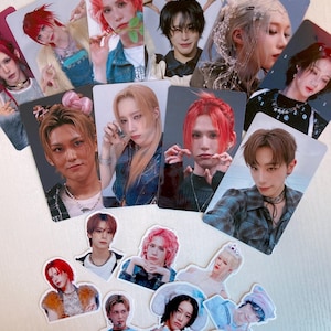 May include: A collection of K-pop idol photo cards and stickers. The cards feature various idols with different hairstyles and outfits. The stickers are of the same idols in various poses. The color palette includes reds, pinks, and blues.