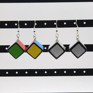 May include: Four pairs of earrings featuring a cube design with different colored sides. The cubes are black with a silver, green, yellow, blue, and red color scheme.